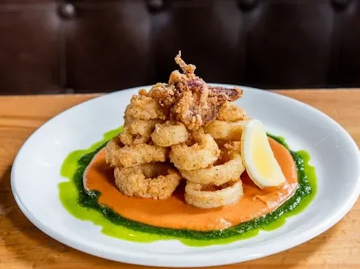 Crispy fried calamari rings and tentacles piled high on a white plate over a bed of orange and green sauces, garnished with a fresh lemon wedge.