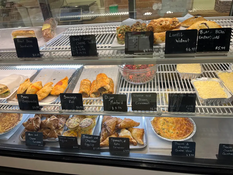 A glass display case at Mabel's Bakery & Specialty Foods filled with savory baked goods, including empanadas, sausage rolls, quiches, and turnovers, each with a small black price tag.