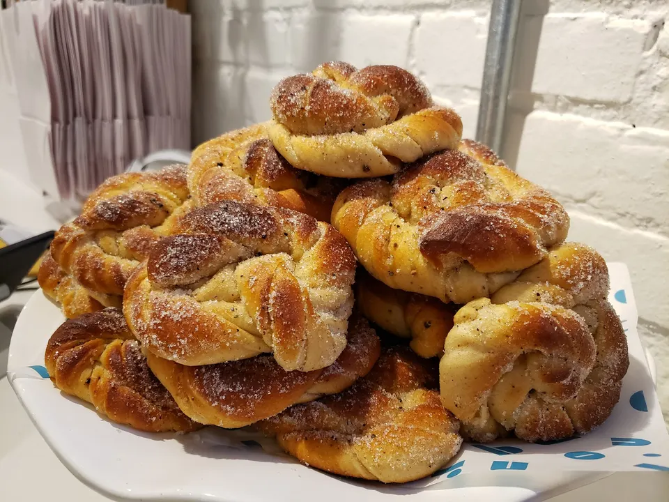A high stack of freshly baked, golden-brown cardamom buns dusted with sugar on a white serving platter.
