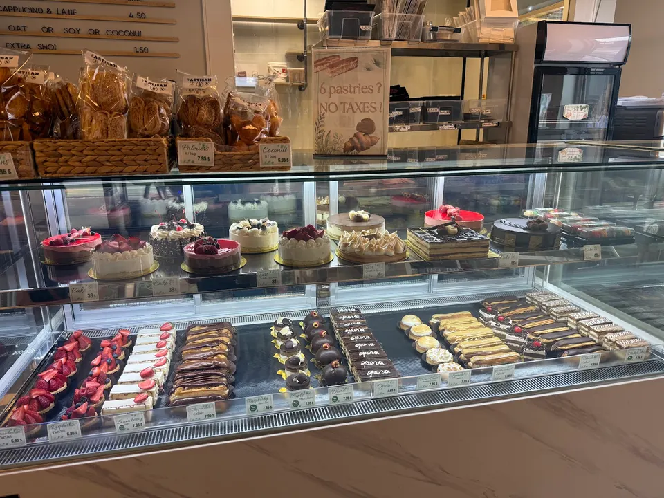 A glass display case filled with a variety of gluten-free pastries, including whole cakes on the top shelf and individual tarts, eclairs, and sliced cakes on the bottom shelf.