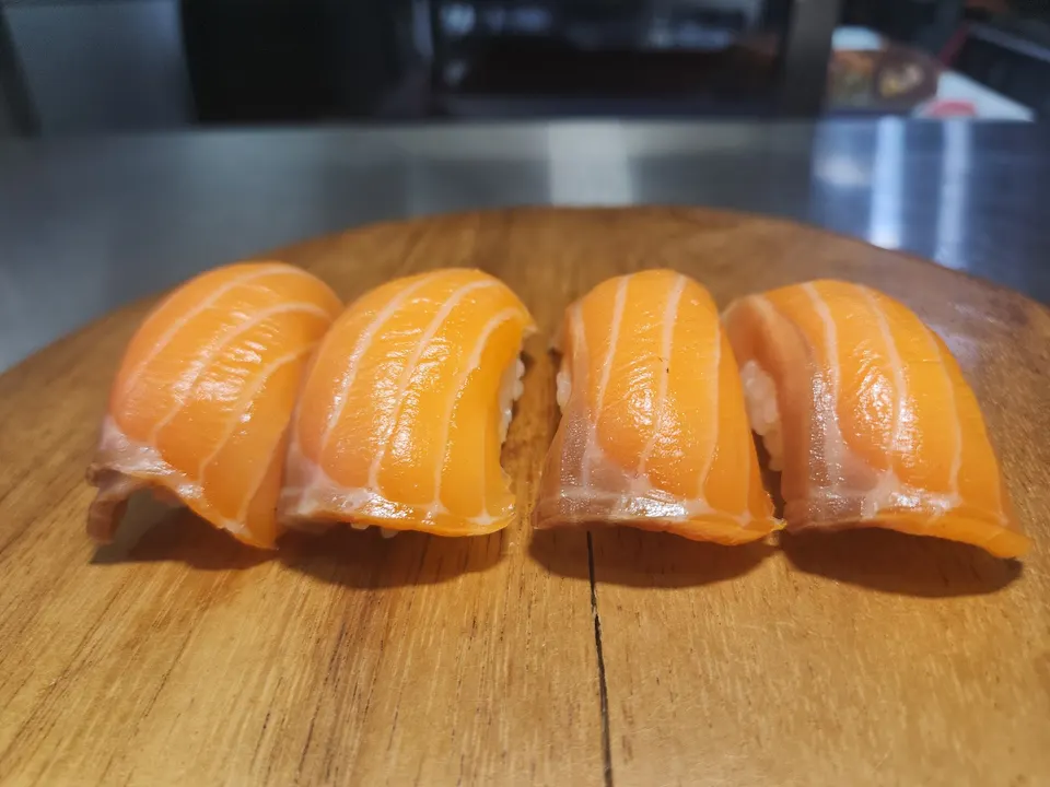 Four pieces of salmon nigiri sushi lined up on a wooden serving board.