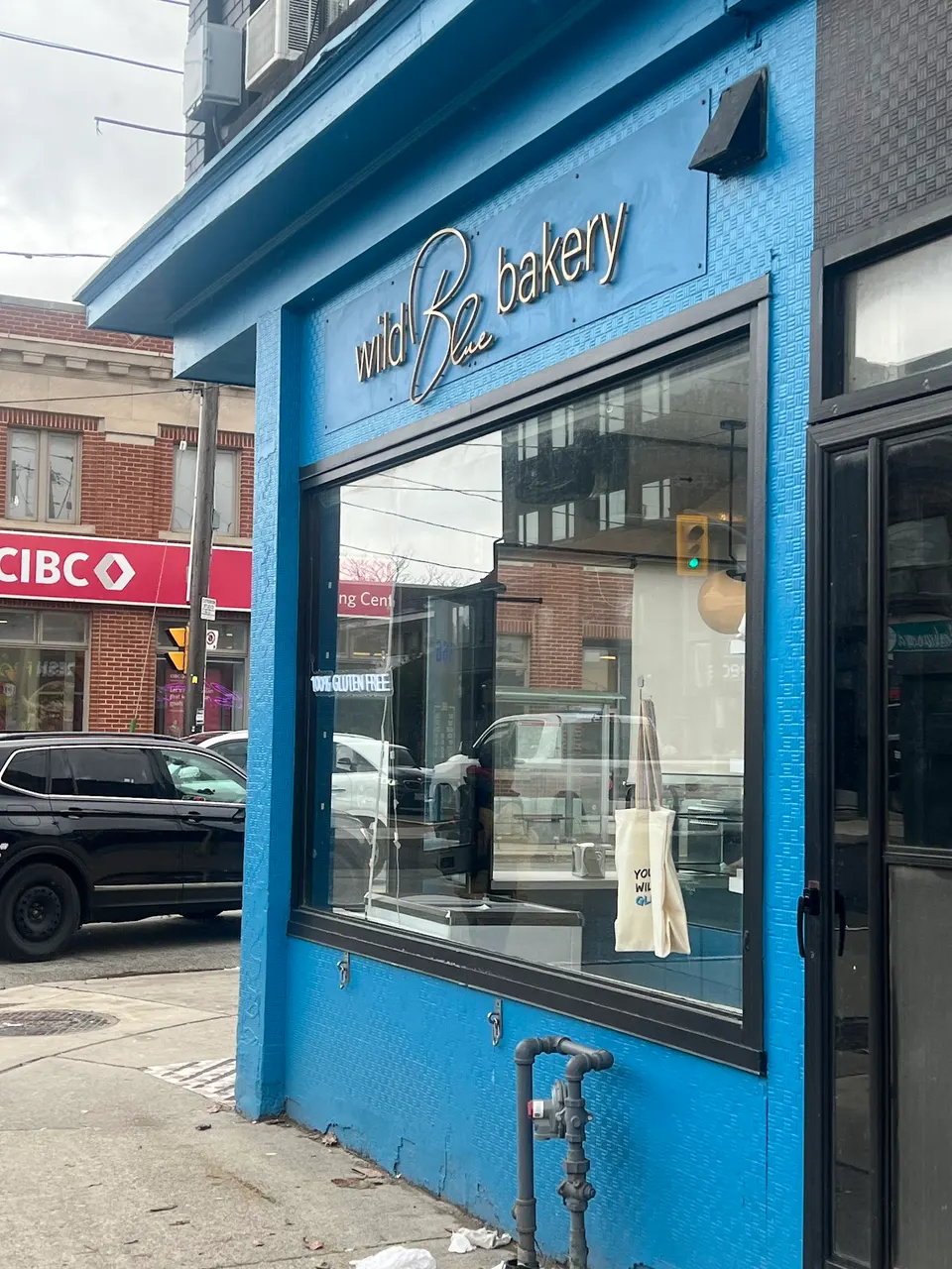 The bright blue exterior storefront of Wild Blue Bakery, featuring a large window displaying a tote bag and a sign that reads 100% Gluten Free.