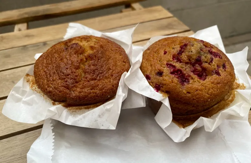 Two freshly baked gluten-free muffins in white paper liners sitting on a wooden table.