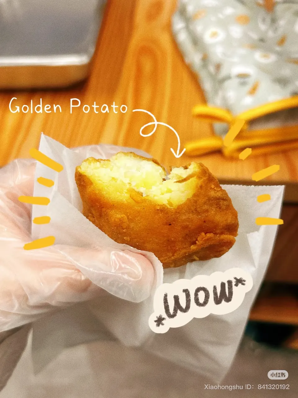 A hand wearing a clear plastic glove holds a bitten, golden-brown fried potato snack wrapped in white paper, showing its fluffy yellow interior.